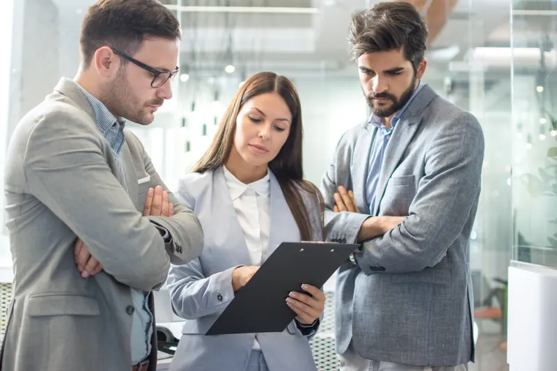 Three people reviewing an audit on a clipboard