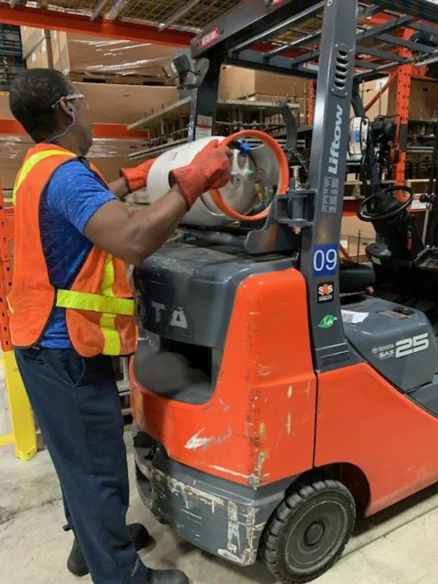 A worker changing the propane cylinder on a forklift