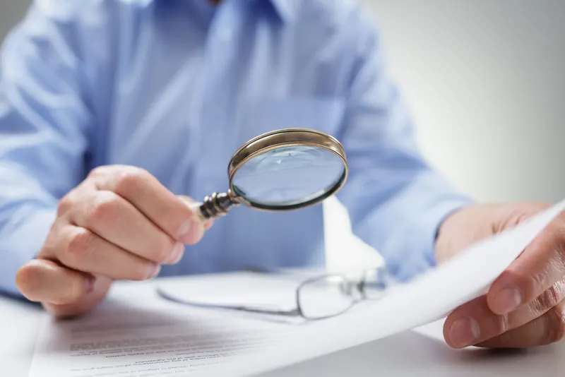 A person reviewing a document through a magnifying glass