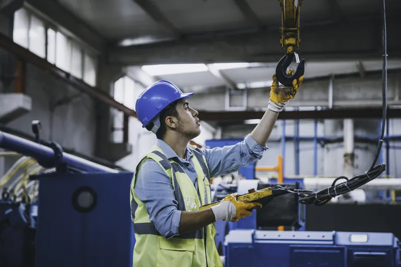 A worker guiding a load on an overhead crane hook