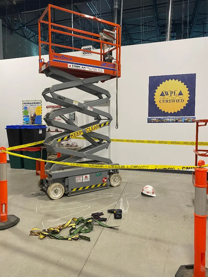 A scissor lift taped off for practical training, with the WPL Certified sign behind it