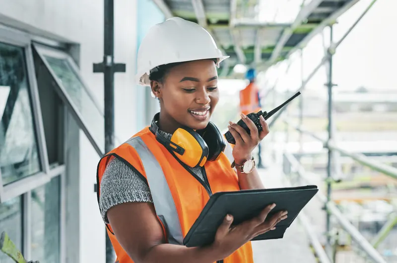 A supervisor in a hard hat and vest checking a tablet on site